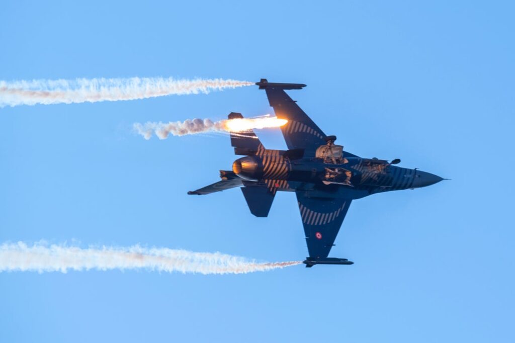 A dynamic image of a jet fighter executing aerial maneuvers with contrails under a bright blue sky.